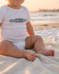 Baby wearing Abnormal Heights onesie on a blanket at the beach in San Diego