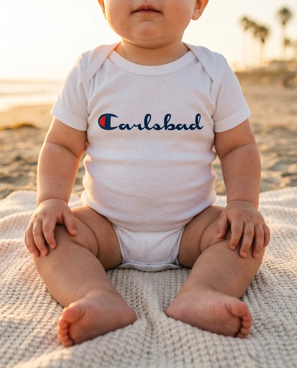 Baby wearing Carlsbad (Champion Parody) bodysuit on a San Diego beach at golden hour