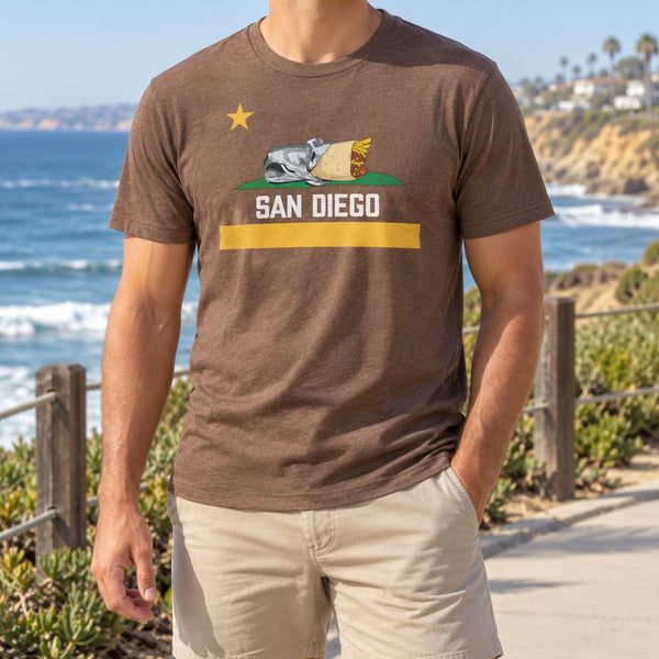 Man wearing a heather brown Padres colors San Diego burrito flag T-shirt on a coastal walkway